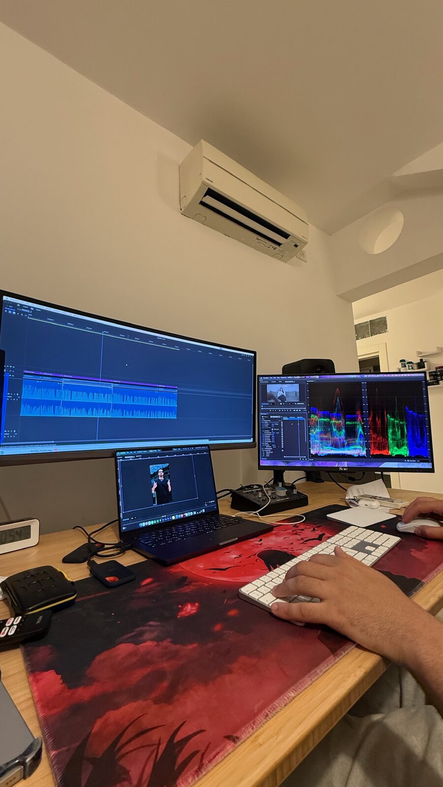 עורך וידאו עובד בעמדת עריכה מתקדמת עם מספר מסכים ולפטופ, בתהליך של פוסט-פרודקשן.