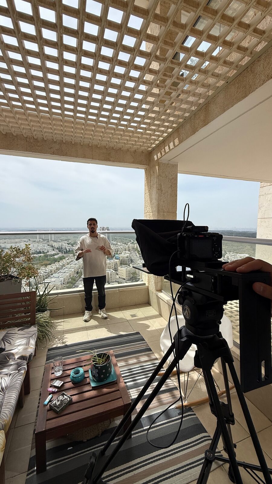 מאחורי הקלעים של יום צילום וידאו שיווקי, עם מצלמה וטלפרומפטר המכוונים אל מרואיין במרפסת המשקיפה לנוף אורבני.